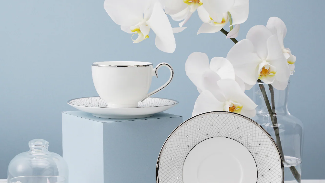 White teacup and saucer set with decorative plate on a light blue background with white orchids.