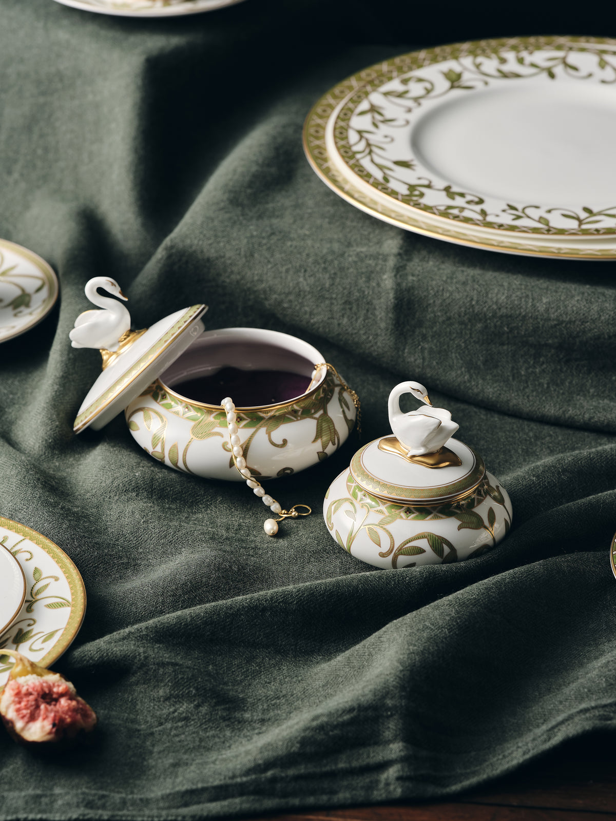 Decorative ceramic containers with swan designs on a green tablecloth.