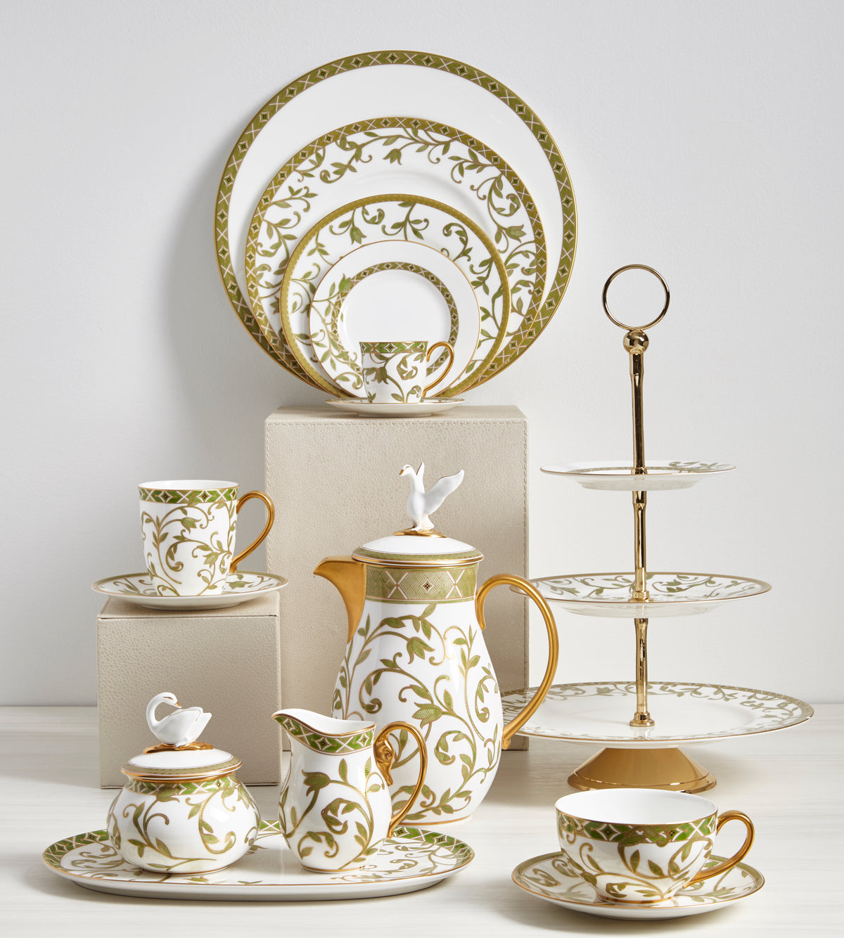 Gold and white ceramic tableware set with a three-tiered stand on a light gray background