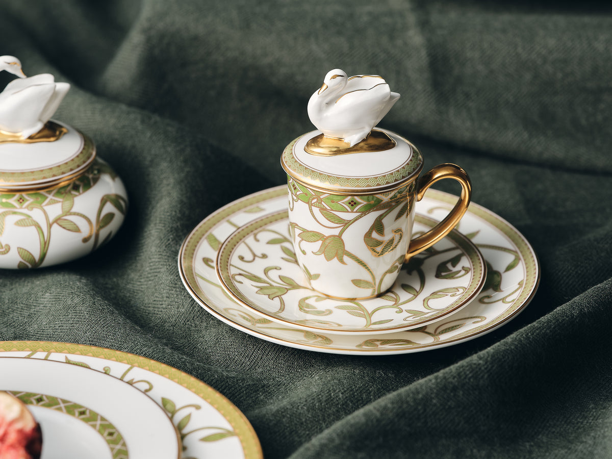 Decorative ceramic cup and saucer with floral design on a green fabric background